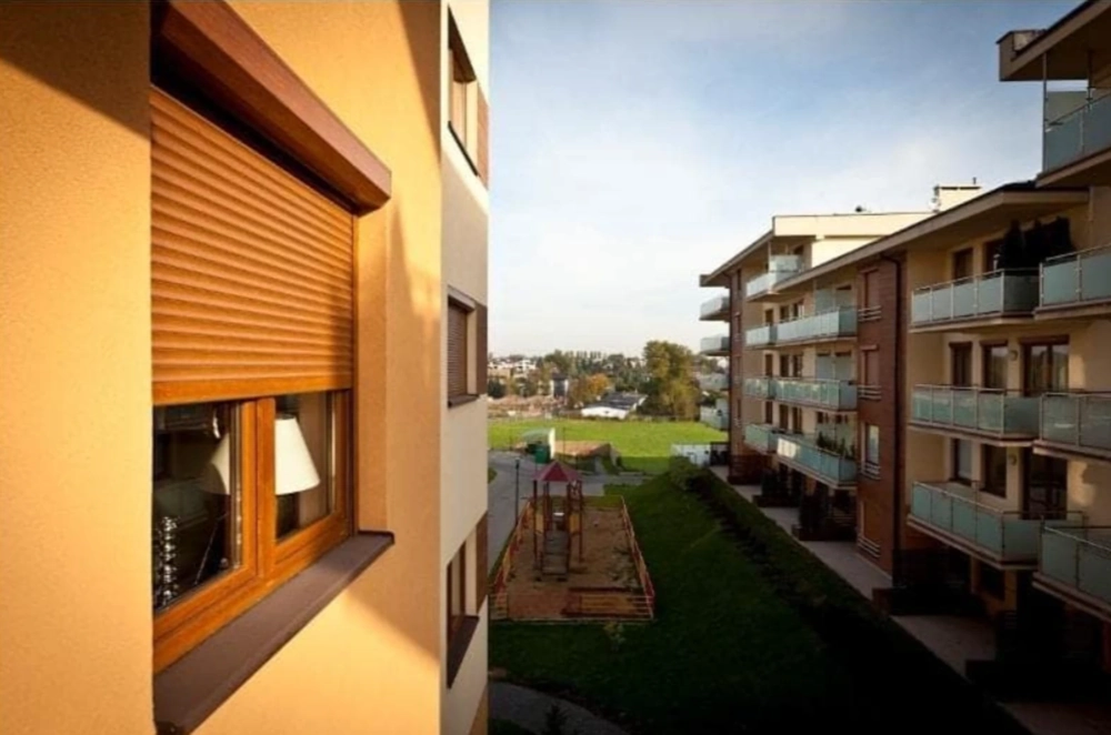 Okno z zamkniętą roletą zewnętrzną w elewacji budynku z widokiem na patio i plac zabaw