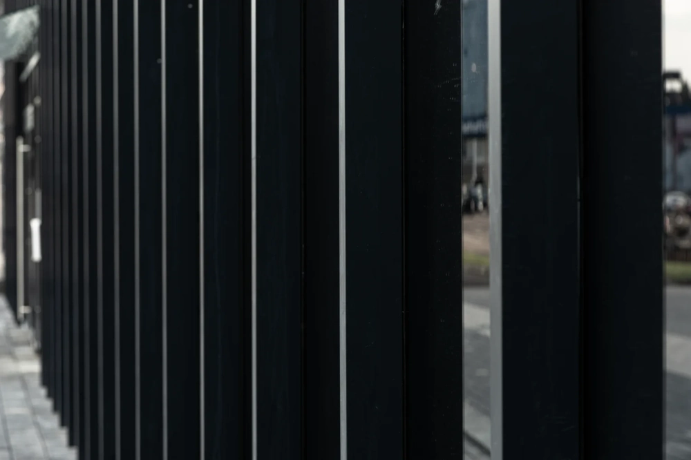 Czarne pionowe aluminiowe słupki ogrodzenia palisadowego na tle podwórza