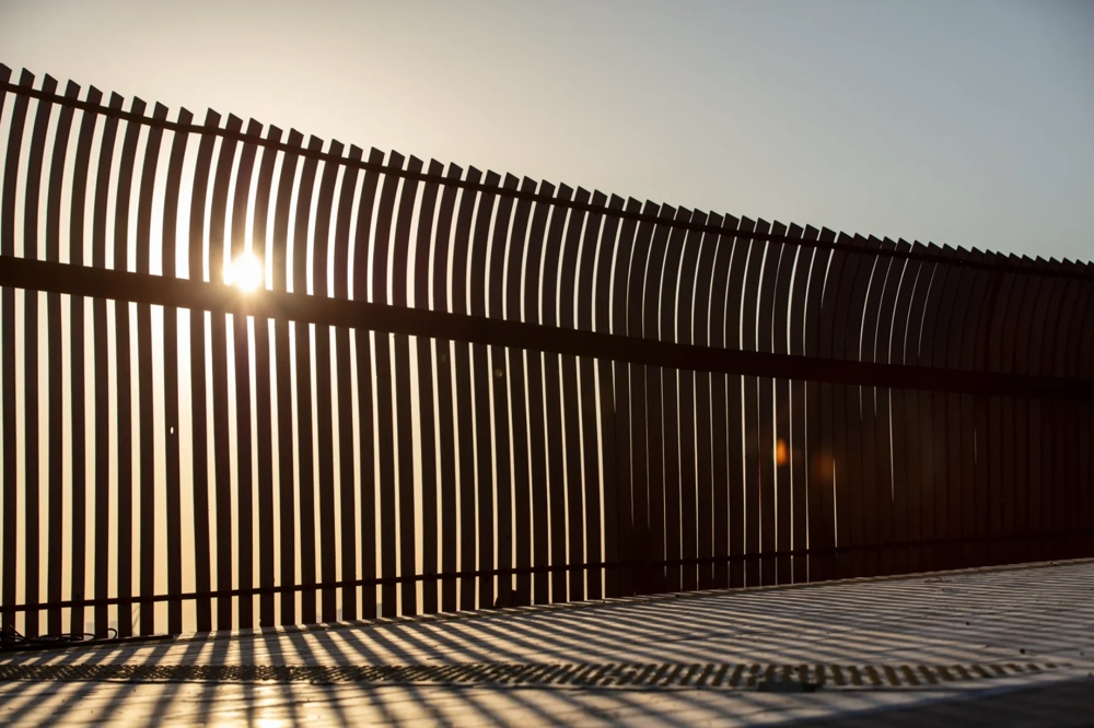 Ogrodzenie palisadowe z pionowymi aluminiowymi lamelami na tle zachodzącego słońca