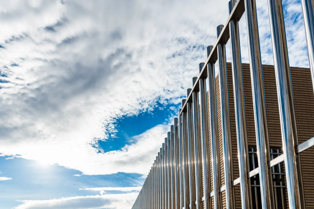 Nowoczesne ogrodzenie palisadowe z aluminiowych pionowych profili na tle nieba