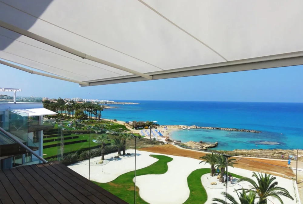 Markiza tarasowa nad balkonem z szklaną balustradą, widok na plażę i turkusowe morze