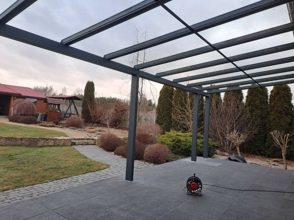 Zadaszenia na taras z aluminiowymi słupami i przeszklonym dachem na kamiennym tarasie